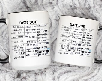 Puede incluir: Una taza de cerámica blanca con asa negra presenta un diseño en blanco y negro con el texto "DATE DUE" y una lista de fechas. La taza es una réplica de una tarjeta de biblioteca vintage.