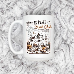 May include: White ceramic mug with a Halloween-themed design. The mug features the text "READ IN PEACE Book Club" and an illustration of skeletons, pumpkins, books, and musical notes. The text "MEETS EVERY TUESDAY IN OCTOBER" is also included.