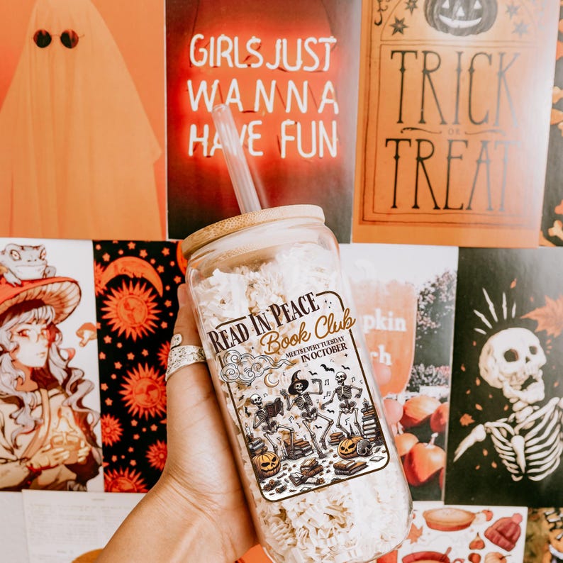 May include: A clear glass jar with a bamboo lid and a straw, displaying a "Read in Peace Book Club" sticker with skeleton illustrations and pumpkins. The background features Halloween-themed posters with text such as "Trick or Treat" and "Girls Just Wanna Have Fun."