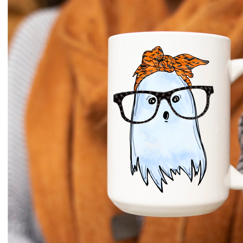 May include: White ceramic mug with a cartoon ghost wearing orange and black patterned glasses and a headband. The ghost has a surprised expression.