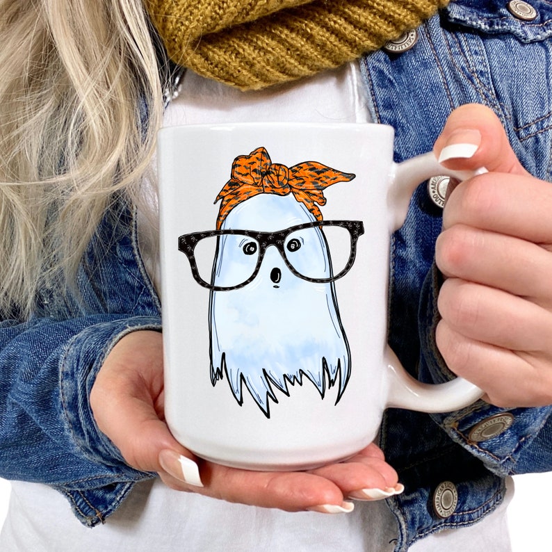 May include: White ceramic mug with a ghost wearing glasses and a black and orange bandana. The ghost has a surprised expression.