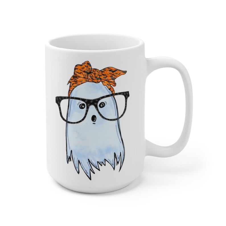 May include: White ceramic coffee mug with a blue ghost wearing orange and black patterned glasses and a headband. The ghost has a surprised expression.