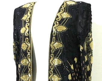 Könnte beinhalten: Eine langärmelige, vorne offene schwarze Jacke mit aufwendigen Goldperlen- und Paillettenstickereien. Das Kleidungsstück zeigt ein sich wiederholendes florales Muster an den Vorderkanten und dichte, detaillierte Perlenverzierungen.