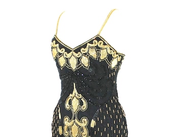 May include: A black sleeveless dress featuring intricate gold beadwork and embroidery in a scrolling pattern. The garment has thin spaghetti straps, a V-neckline, and a fitted silhouette with a front slit, adorned with vertical beaded lines.