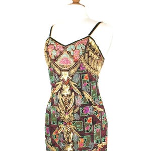 May include: A sleeveless midi dress featuring a dark maroon base with a geometric grid pattern. The dress is heavily embellished with gold, pink, teal, and silver sequins and beads in intricate floral and abstract motifs, with thin straps.