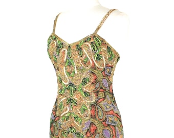 May include: A sleeveless knee-length dress featuring an intricate pattern of gold, green, and purple beads and sequins. The garment has thin shoulder straps, a sweetheart neckline, and a front slit that reveals a solid black lining underneath.
