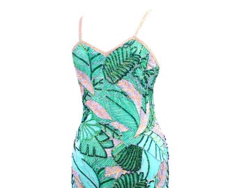 Può includere: Un abito midi senza maniche con un vivace motivo a foglie tropicali nei toni del verde, ottanio e rosa tenue. L'intera superficie è riccamente decorata con intricate perline e paillettes, con spalline sottili e uno scollo a V.