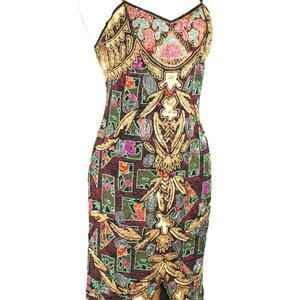 May include: A sleeveless midi dress in a deep burgundy hue, featuring an intricate pattern of geometric shapes and floral motifs. The garment is heavily embellished with gold, pink, blue, and green sequins and beads, with a V-neckline and thin straps.