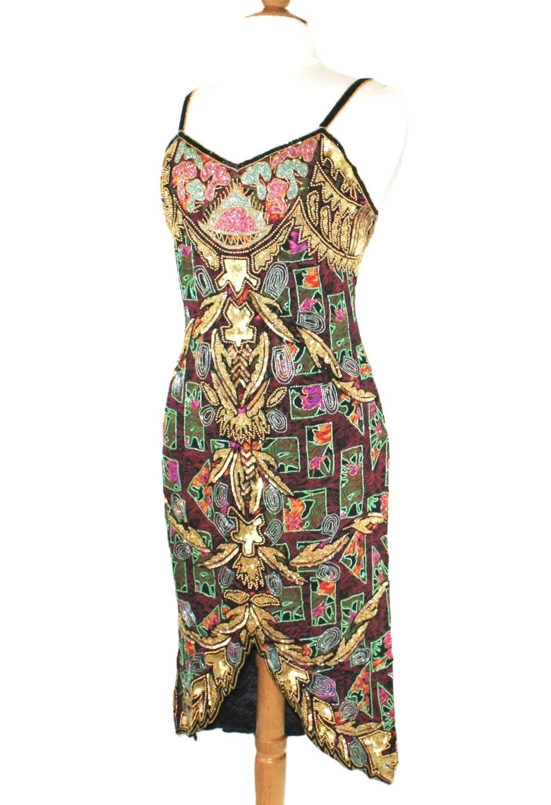 May include: A sleeveless midi dress featuring a dark maroon base with a geometric grid pattern. The dress is heavily embellished with gold, pink, teal, and silver sequins and beads in intricate floral and abstract motifs, with thin straps.