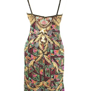 May include: A sleeveless sheath dress featuring a dark burgundy base with a geometric pattern in green, pink, and black. The garment is heavily embellished with gold sequins and beads in intricate floral and scroll motifs along the bodice and hem.
