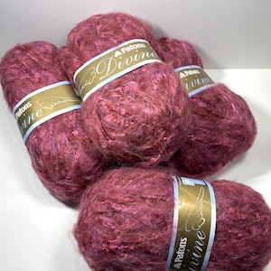 May include: Close-up of five balls of Patons Divine yarn in shades of pink and burgundy. Each ball has a label with the brand name and the word "Divine" in a script font. The yarn appears soft and textured, ideal for knitting or crochet projects.