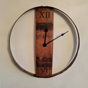 Könnte beinhalten: Eine rustikale Wanduhr mit einem Holzgesicht und einem Metallring. Das Zifferblatt besteht aus einem Stück Holz mit den römischen Ziffern XII und VI. Die Zeiger der Uhr sind schwarz.