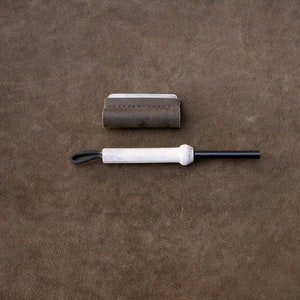 May include: A brown leather case with a black metal fire starter rod with a white handle and a black lanyard.