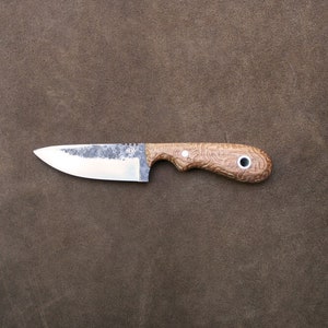 Puede incluir: Un pequeño cuchillo de hoja fija con mango de madera marrón y hoja plateada. El mango tiene un patrón decorativo y un pequeño agujero.