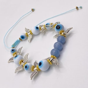 May include: A light blue adjustable bracelet featuring a series of white and blue evil eye beads, interspersed with silver-colored wing charms and gold accents. The bracelet also includes blue-grey beads.