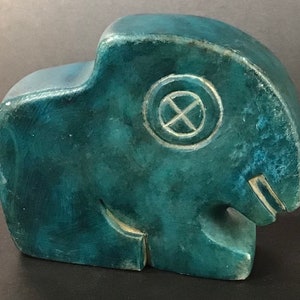 May include: A teal green carved stone sculpture of an abstract animal with a circular design on its head.