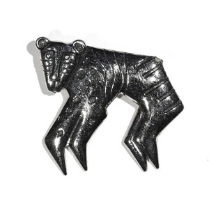 May include: A silver-toned metal brooch in the shape of a stylized animal, possibly a bear or a dog. The brooch has a detailed design with geometric shapes and a textured surface.