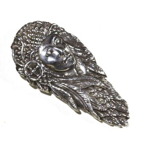May include: A silver pendant featuring a detailed sculpted face of a woman with a crown of leaves and feathers.