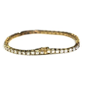 May include: A gold tennis bracelet with a row of small, clear diamonds.