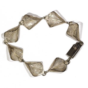 May include: A silver bracelet with a delicate, intricate design. The bracelet is made up of a series of connected, diamond-shaped links, each featuring a delicate, filigree pattern.