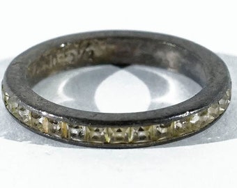 May include: A silver band ring with a row of clear square-shaped stones around the entire band.