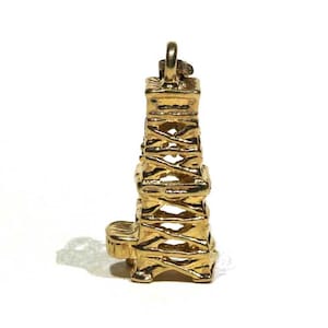 May include: A gold-colored charm in the shape of an oil derrick. The charm is detailed and has a textured surface.