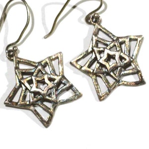 May include: A pair of silver star-shaped earrings with a geometric design. The earrings are made of a metal that has a slightly iridescent finish.