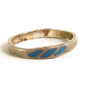 May include: A silver ring with three blue enamel leaf-shaped designs. The ring has a slightly tarnished appearance, suggesting age or wear. The band is simple and thin, with a classic design.
