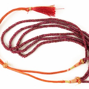 May include: A strand of ruby red gemstone beads with a red tassel on one end and two gold tassels on the other end. The beads are strung on a red cord.