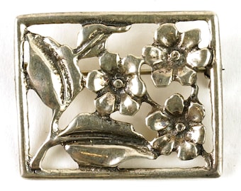 May include: A silver brooch with a square frame and a design of three stylized flowers with leaves.