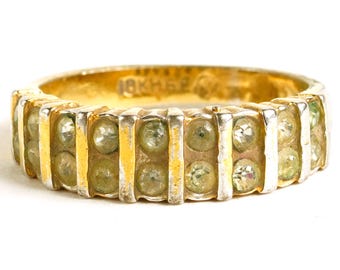 May include: A gold-toned ring with two rows of small, round, light green gemstones. The ring has a textured design with vertical silver-colored bars separating the gemstones. The inscription "18K HGE" is visible on the ring's band.