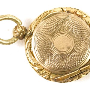 May include: A gold locket with an ornate design and a hinged lid. The locket has a loop for attaching a chain.