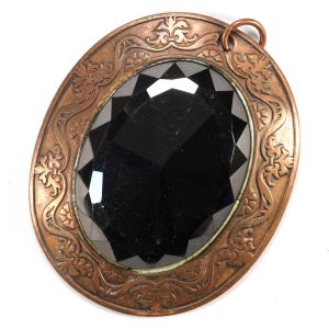 May include: An oval-shaped copper pendant with an ornate design featuring a black faceted glass stone in the center.