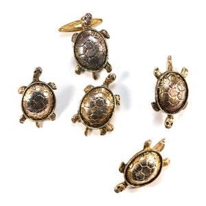 May include: Set of five gold-tone turtle cufflinks. Each cufflink features a detailed turtle design with a textured shell.