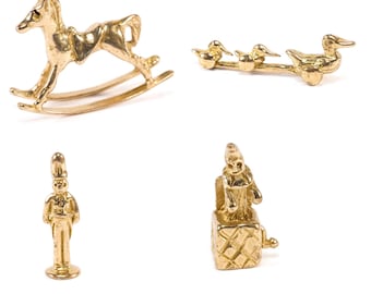 May include: A set of four gold-toned miniature figurines: a rocking horse, a toy soldier, a jack-in-the-box, and a trio of ducks pulling a wagon.