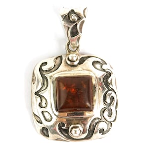 May include: A silver pendant with an ornate design. The pendant features a square, amber-colored stone set in a decorative frame. The silver has a detailed, swirling pattern around the stone and at the top for the chain.