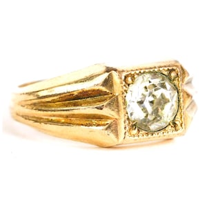 May include: A gold ring with a large, round, clear gemstone set in a square bezel. The ring band has a ridged design. The ring is a classic style, suitable for various occasions.