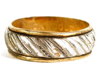 May include: A gold and silver-toned ring with a textured, diagonal pattern around the band. The ring has a gold interior and edges, with a silver-colored central band. The design features a repeating, ridged pattern.