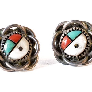 May include: A pair of silver earrings with a circular design featuring turquoise, red coral, and white shell inlay. The earrings have a woven, knot-like design around the edges.
