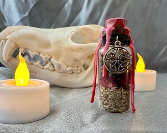 May include: A small glass bottle with a red wax seal and a gold charm. The bottle is filled with dried herbs and flowers. The bottle is sitting on a white surface next to a white candle.