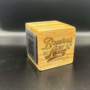 May include: A wooden coaster with a metal plate featuring a QR code and the text "Main Menu". The coaster also has the text "Brewer's Alley" with a stylized font, "EST. 1996", and "Frederick, MD".