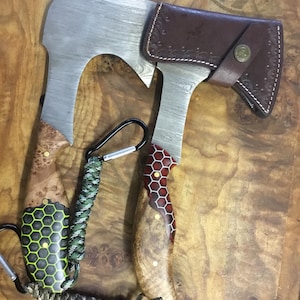 May include: Two hand-crafted axes with unique wooden handles. The handles are made of wood with a honeycomb pattern and a brown leather sheath.