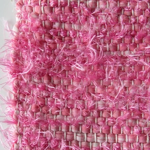 Puede incluir: Tela tejida rosa con una textura peluda. La tela tiene un patrón tejido y está hecha de un material suave y esponjoso.