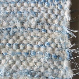 Puede incluir: Primer plano de una tela tejida con un patrón azul y blanco. La tela tiene una superficie texturizada y un borde deshilachado.