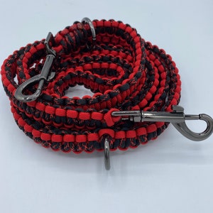 May include: A red and black braided dog leash with gunmetal-colored hardware. The leash is coiled and features a swivel clasp and a D-ring for attaching accessories. The leash is made of durable, woven material.