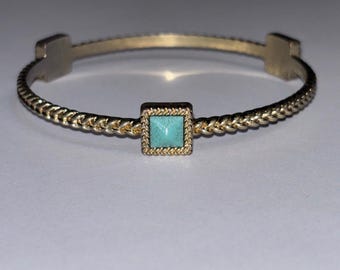 May include: Gold-toned bangle bracelet with a square turquoise stone centerpiece. The bracelet features a braided rope design and square end caps. A stylish piece of jewelry.