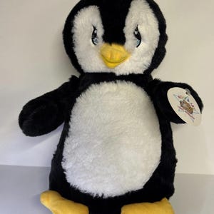 May include: A plush penguin toy with a black head, wings, and back, and a white chest. It has a yellow beak and feet, and blue eyes. A tag is attached to the right wing. The penguin is designed to look like a cartoon character.