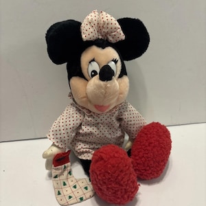 May include: A plush Minnie Mouse doll with black ears, a pink bow with red polka dots, and a pink and white polka dot dress. The doll has red fuzzy feet and a Christmas stocking.