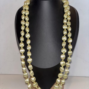 Può includere: Una collana a doppia fila con grandi perle giallo pallido. Le perle hanno una forma leggermente irregolare e sono infilate con piccoli distanziatori color oro. La collana è esposta su un busto di manichino nero su sfondo bianco.