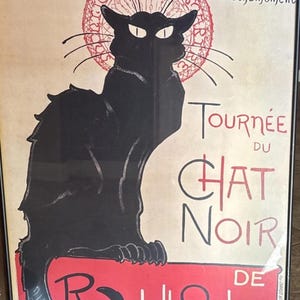 May include: Framed vintage poster featuring a black cat silhouette with glowing eyes. The poster includes French text, including "Tournée du Chat Noir" and "Rodolphe Salis," set against a cream background with red accents. A classic piece of art.